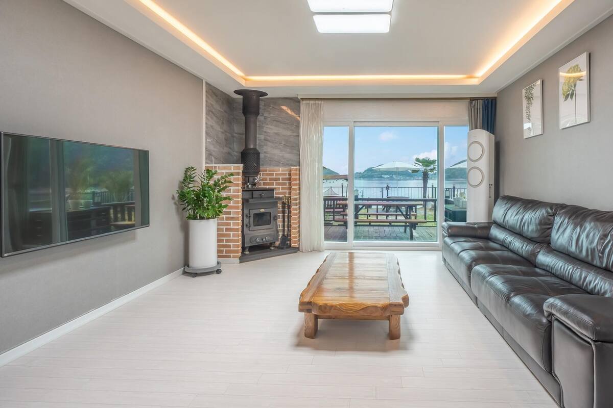 Una sala de estar moderna con chimenea, un sofá de cuero, una mesa de centro de madera y un amplio ventanal con vistas al exterior.