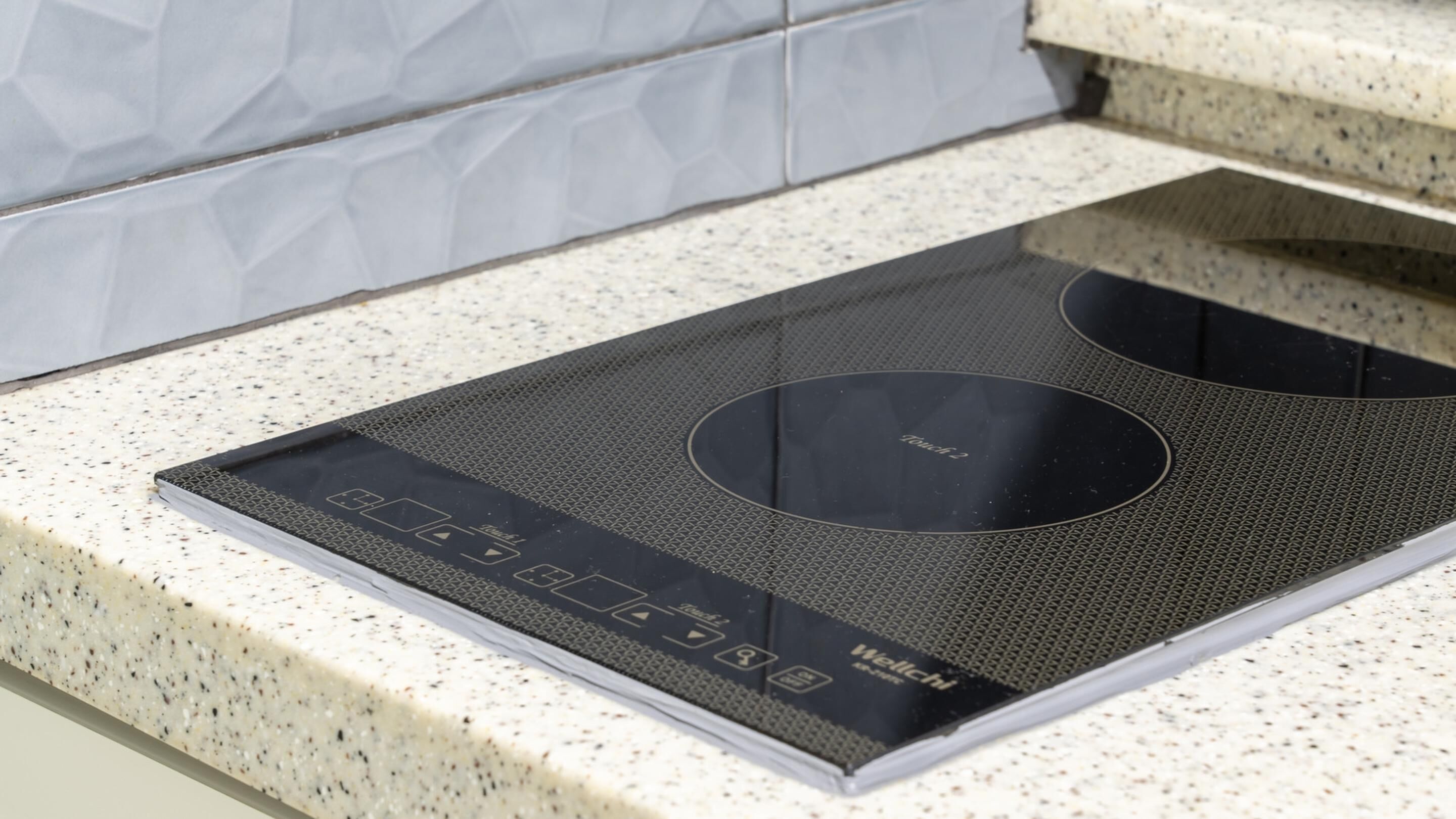 Una cocina de inducción con control táctil y una interfaz digital, ubicada sobre una encimera con vetas.