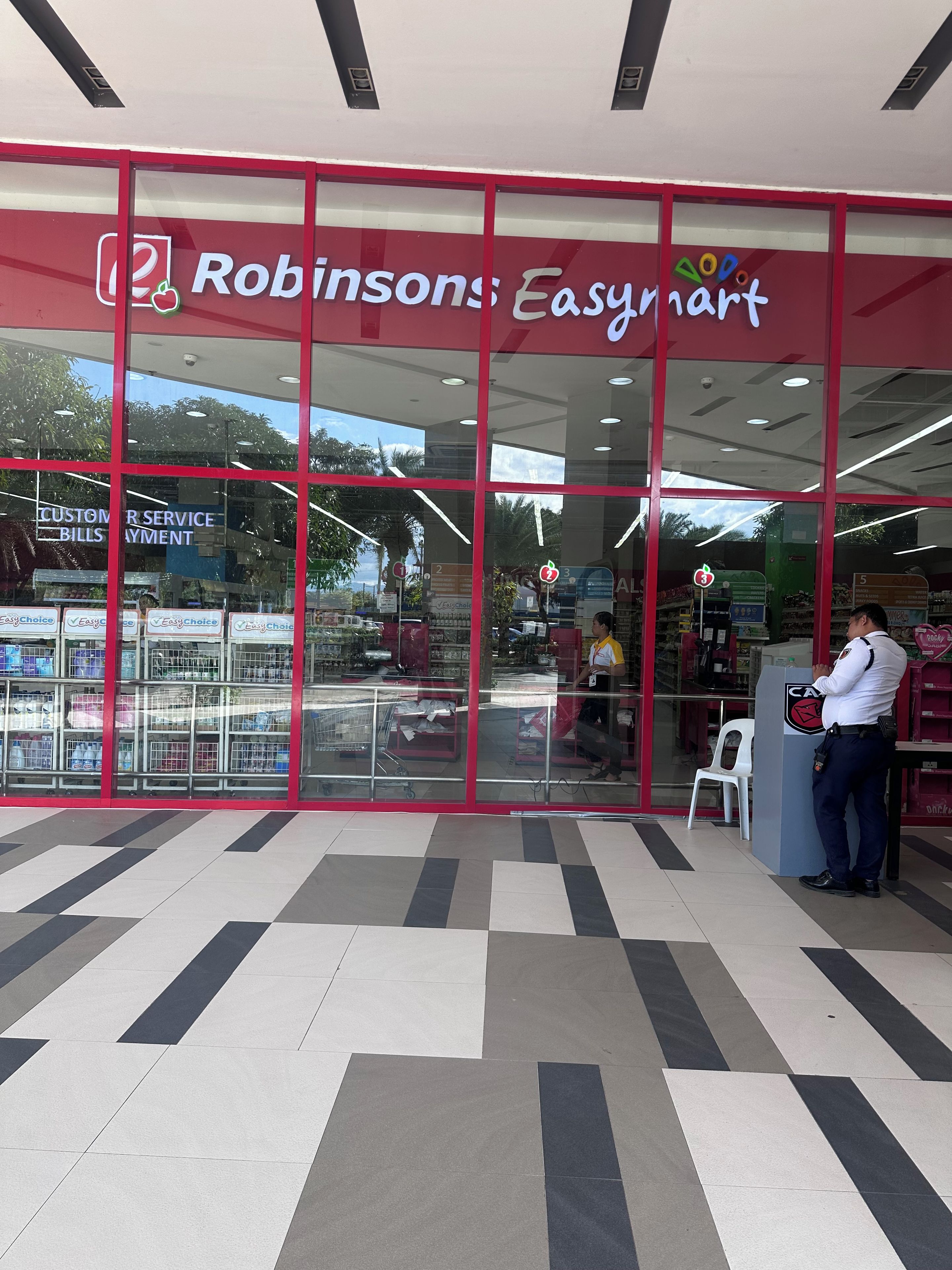 A Robinsons Easymart store with a customer service counter, shopping carts, and a security officer.