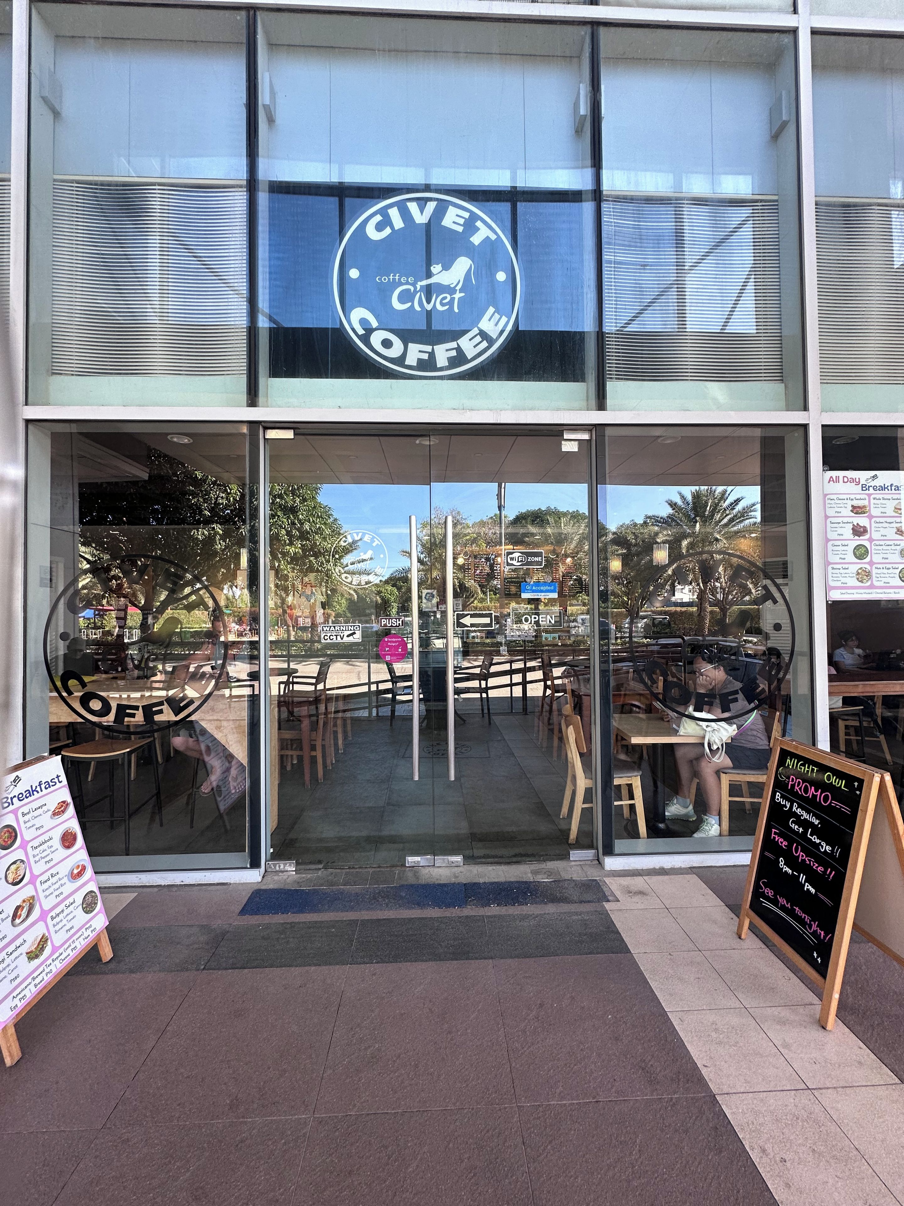 En butik med ett skyltfönster och en skylt som visar texten ”Civet Coffee” samt en menytavla utanför.