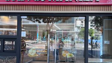 A storefront with a sign reading 'PAN DE MANILA' and a display window showcasing baked goods.