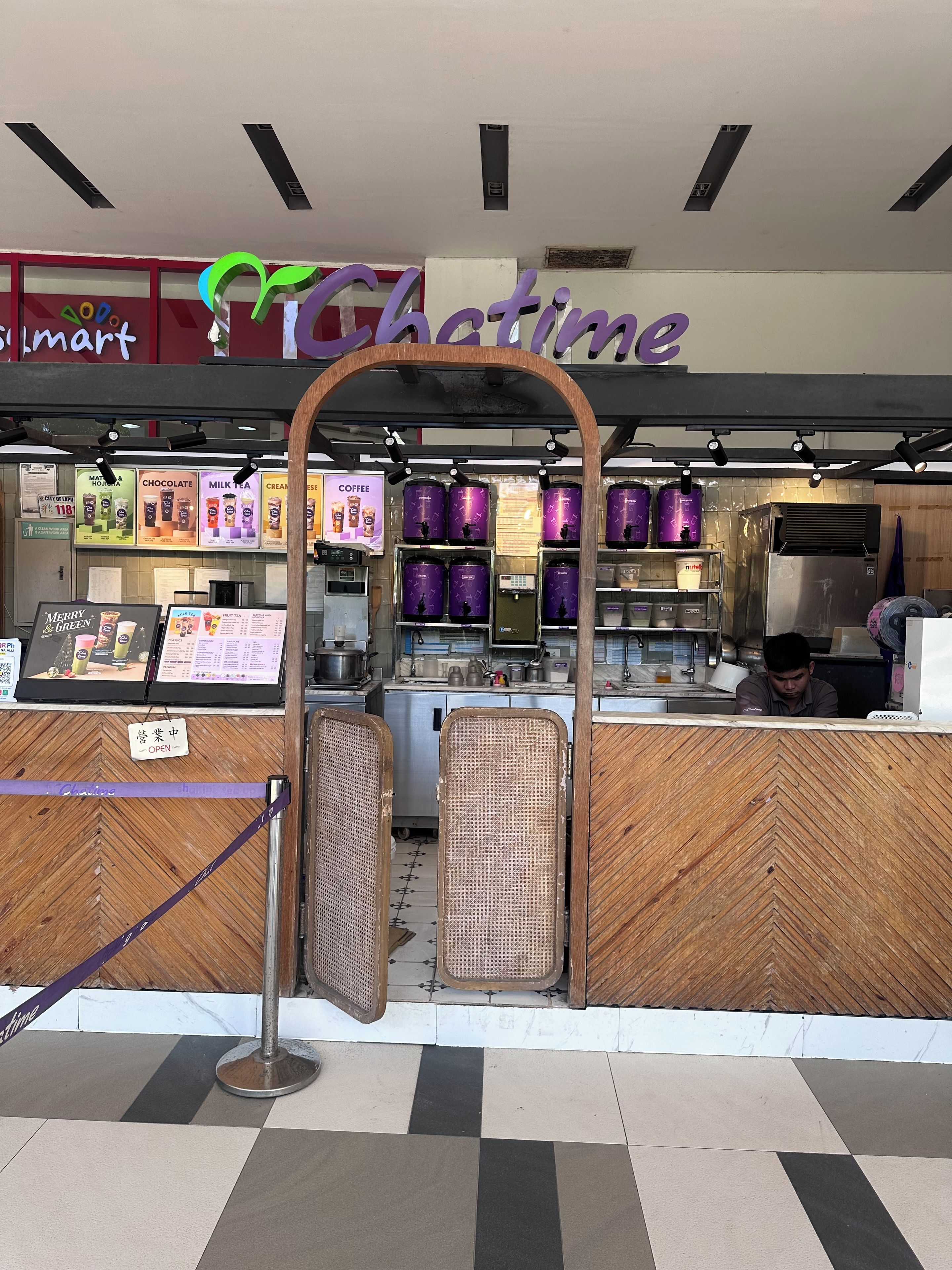 Un café avec un comptoir, des panneaux affichant le menu et une enseigne indiquant « Glatime ».