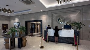 A modern hotel lobby with a reception desk, potted plants, a marble counter, and a large abstract artwork on the wall. - MACTAN NEWTOWN OMP FAMILY ROOM (Lapu-Lapu)