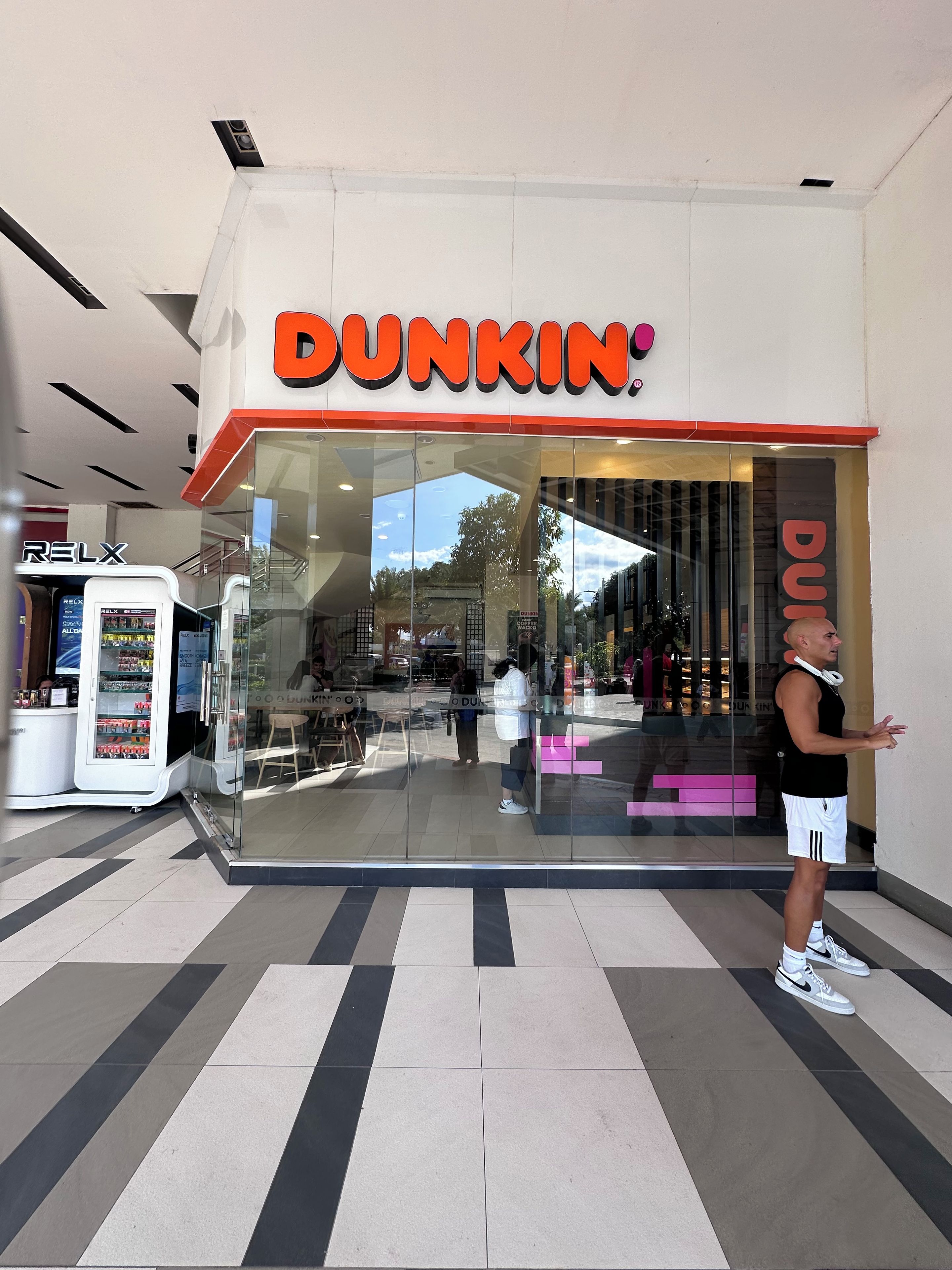 Een Dunkin' Donuts winkel met een glazen voorgevel, een zitgedeelte binnen en een persoon die buiten staat.