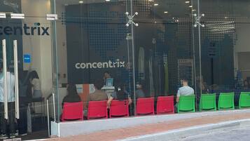 Un magasin Concentrix avec une façade en verre, des chaises rouges et vertes à l’extérieur et une entrée bien visible.