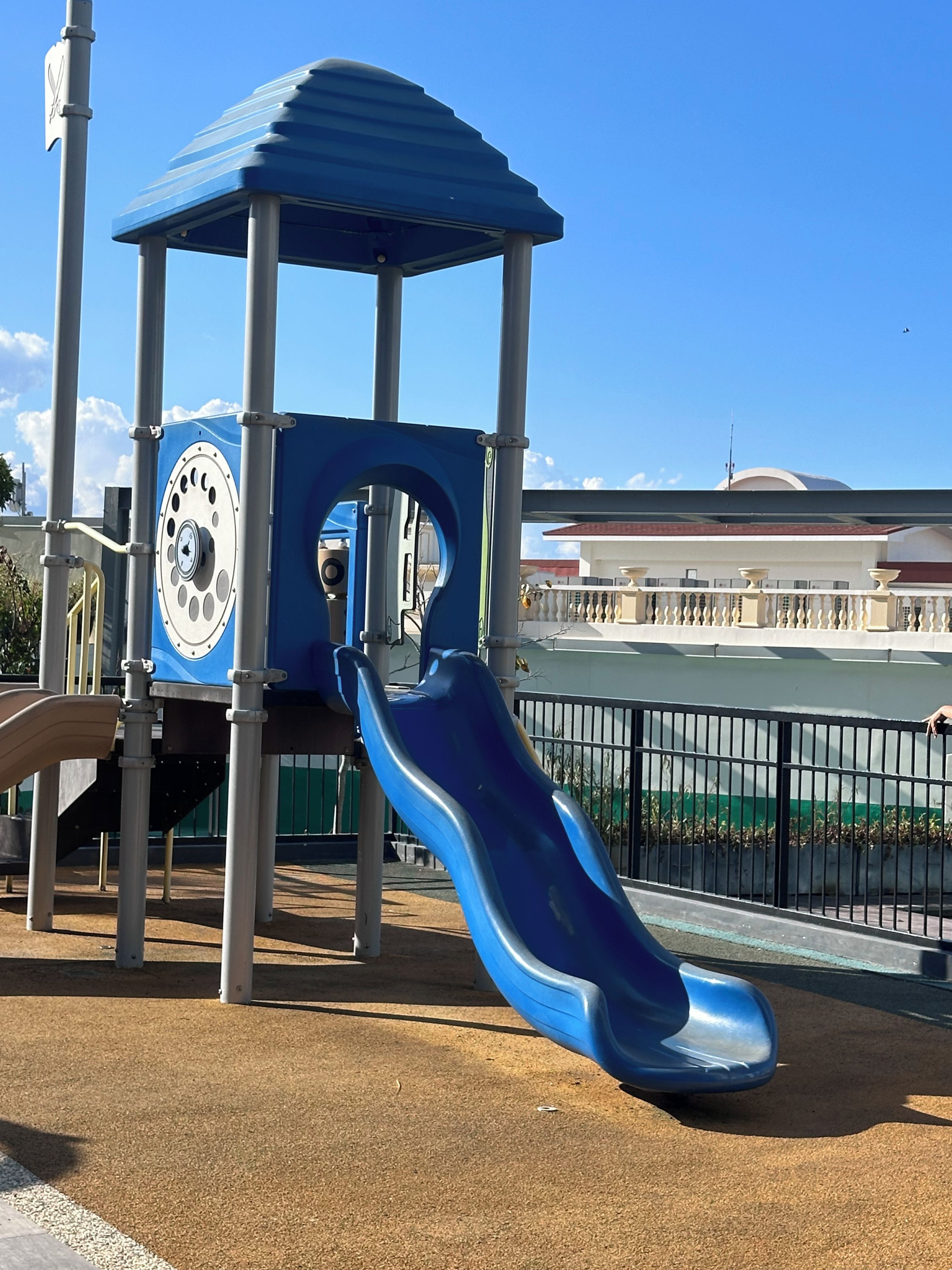 Un parque infantil con un tobogán azul y una estructura de juegos cubierta.