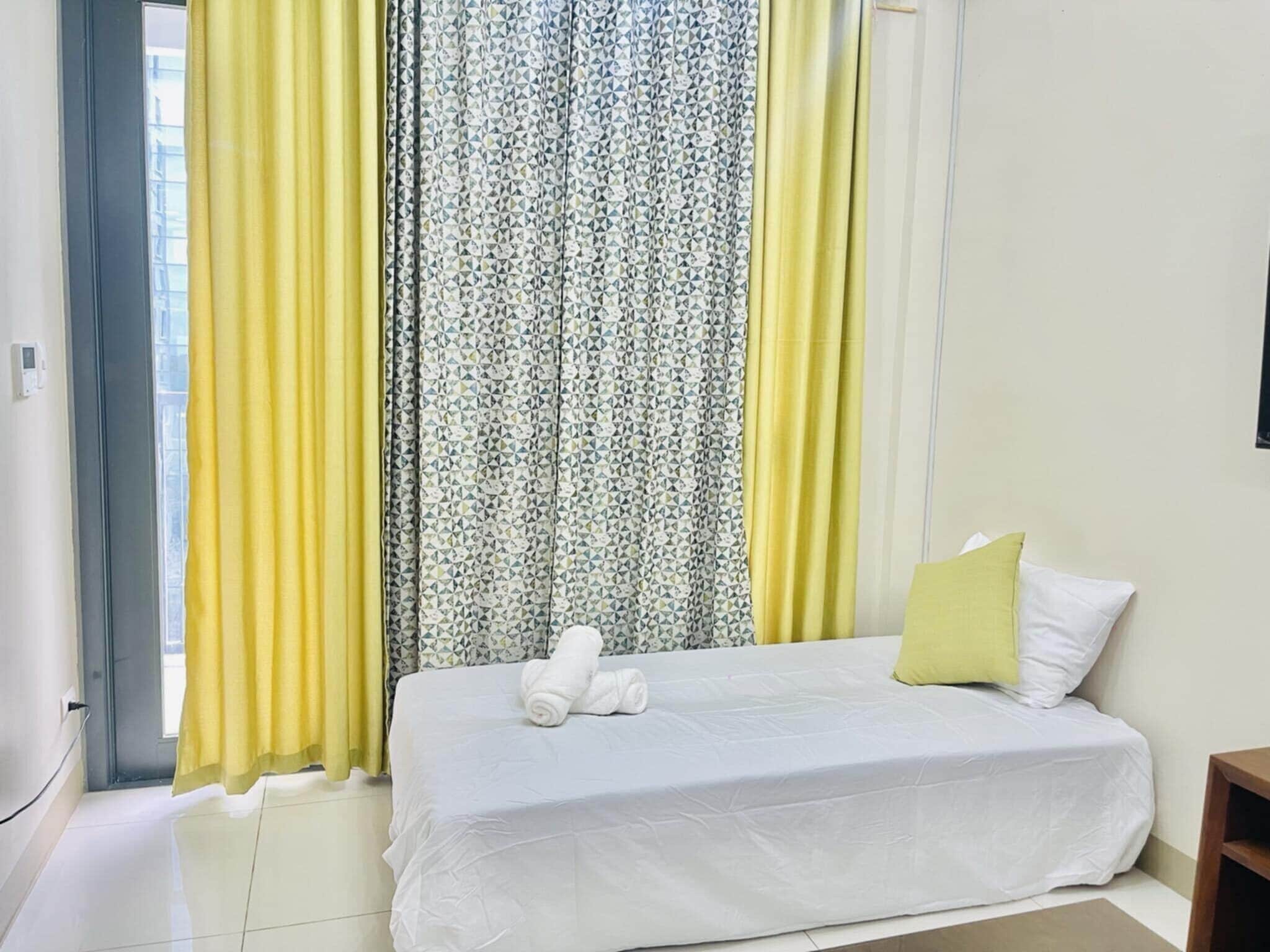 Une chambre d’hôtel avec un lit, une fenêtre avec des rideaux jaunes et un autre rideau à motifs.