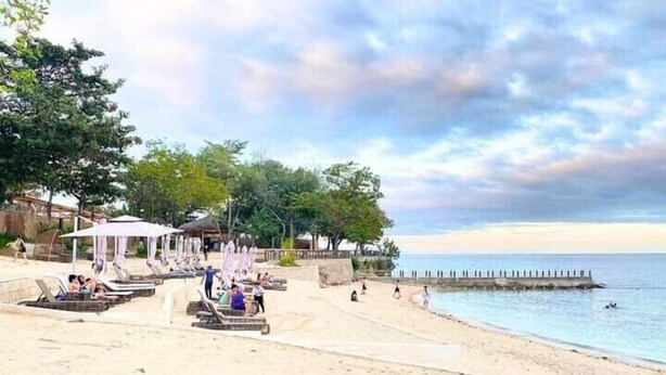 A beach with sun loungers, umbrellas, and a pier extending into the water. - MACTAN NEWTOWN OMP FAMILY ROOM (Lapu-Lapu)