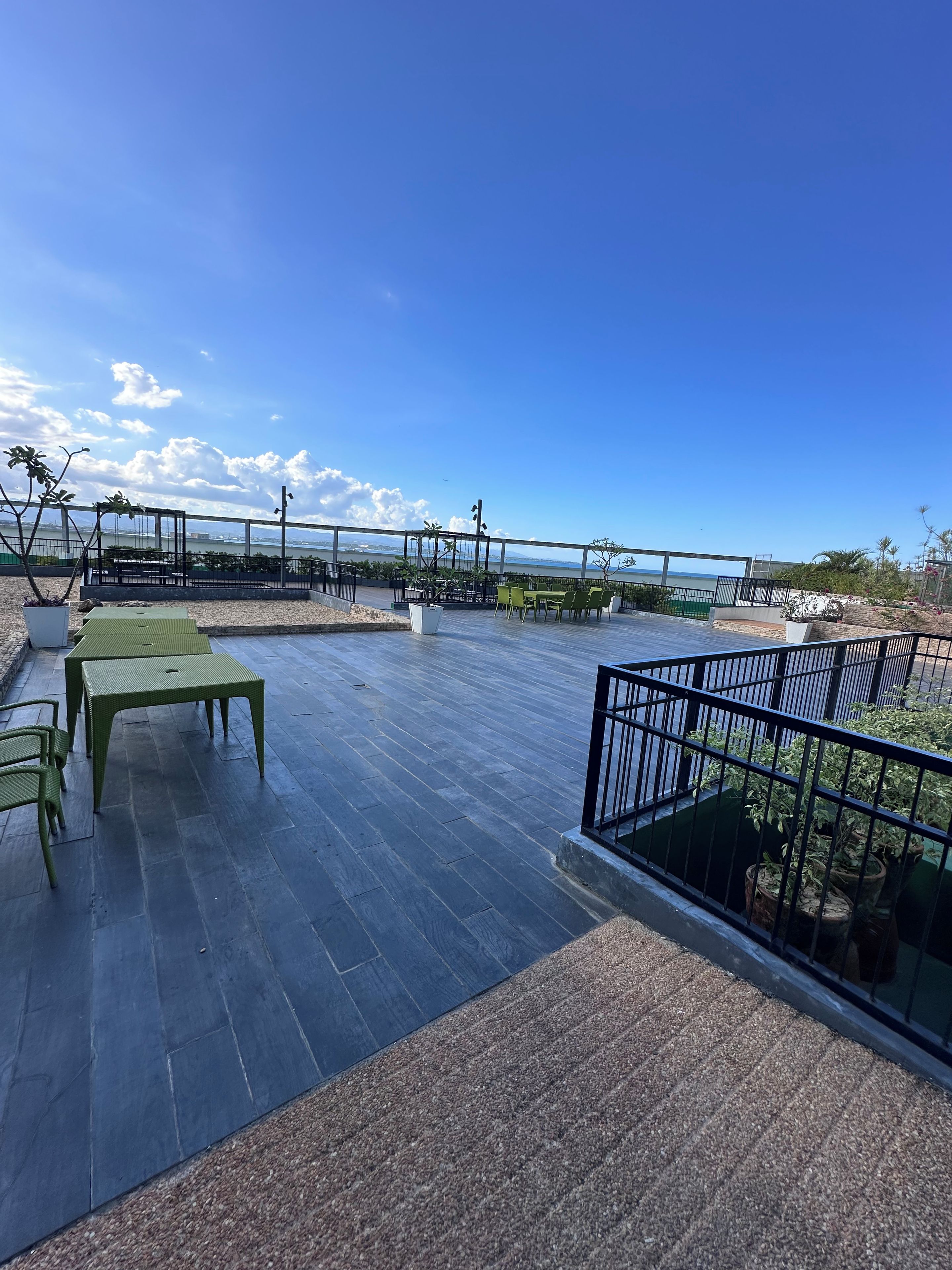 Een terras buiten met uitzicht op zee, met een tafel, stoelen, een balustrade en potplanten.
