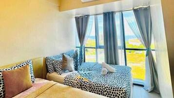 A hotel room with two beds, a ceiling fan, an air conditioning unit, and a view of the outdoors through large windows.