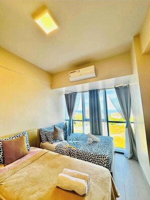 Une chambre d’hôtel avec deux lits, un ventilateur de plafond, un appareil de climatisation et une vue sur l’extérieur grâce à de grandes fenêtres.