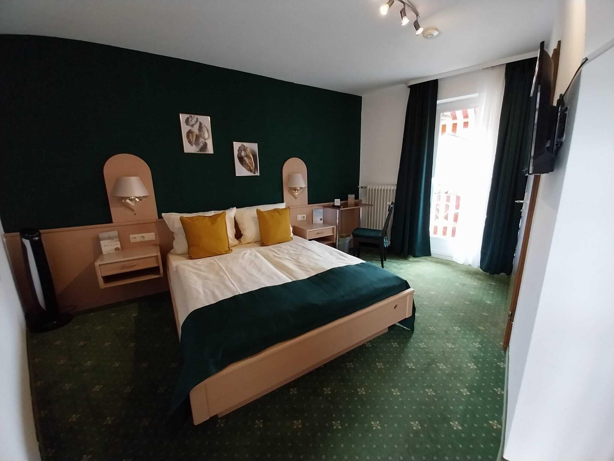 Een hotelkamer met een groot bed, twee nachtkastjes, een bureau en een stoel. Er zijn twee wandlampen en een raam met gordijnen.