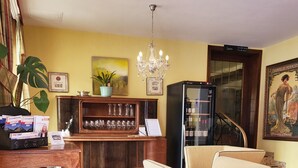A living room with a beige armchair, a wooden coffee table, a chandelier, a refrigerator, and a bookshelf. - Hotel Rüdesheimer Hof (Ruedesheim am Rhein)