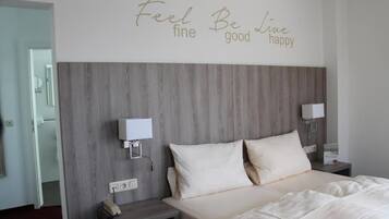 Ein Schlafzimmer mit hölzernem Kopfteil, zwei Nachttischen, einem Bett mit weißer Bettwäsche und einem motivierenden Zitat an der Wand.