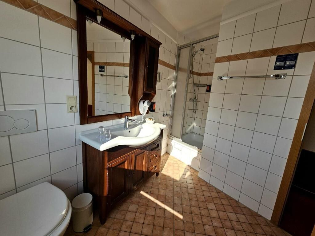 A bathroom with a white sink, wooden vanity, and a shower area.