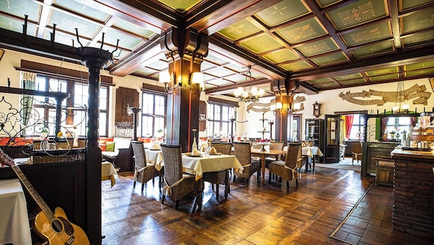 A spacious dining area with wooden floors, high ceilings, and large windows. Tables are set with white tablecloths and surrounded by wicker chairs. - Hotel Rüdesheimer Hof (Ruedesheim am Rhein)