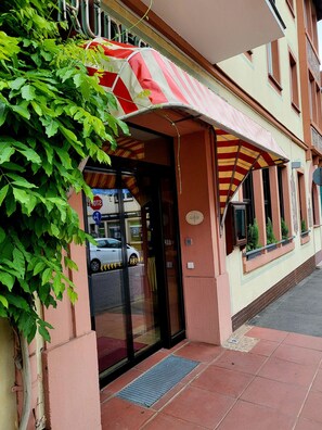 A building with a red and white striped awning, a glass door entrance, and a small window with plants.