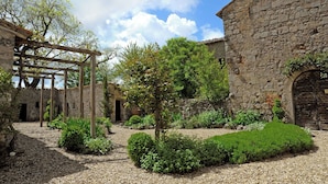 Un patio con paredes de piedra, una pérgola de madera y abundante vegetación.