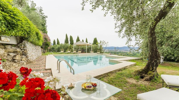 An outdoor swimming pool with a stone wall, a covered seating area, and a table with a drink and fruit. - Wonderful  villa with private pool, WIFI, A/C, TV, terrace, pets allowed and panoramic view (Pistoia)