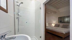 Une salle de bain moderne avec une douche à l’italienne en verre, un lavabo blanc et une pomme de douche visible.