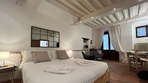 Une chambre avec un grand lit, un bureau et une chaise. Il y a un miroir au mur et une fenêtre avec des rideaux.