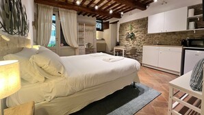 A bedroom with a large bed, a desk, and a kitchenette.
