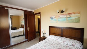 Un dormitorio con cama, mesita de noche, espejo y puerta que da a otra habitación.