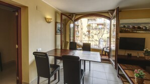 Un comedor con una mesa y sillas de madera, un televisor y vistas a un edificio con balcones.