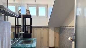 A bathroom with a glass sink, a toilet, and a shower area. There are cabinets and a towel rack visible.