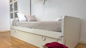 A single-bed room with a checkered bedspread, a white headboard, and a woven basket on the floor.