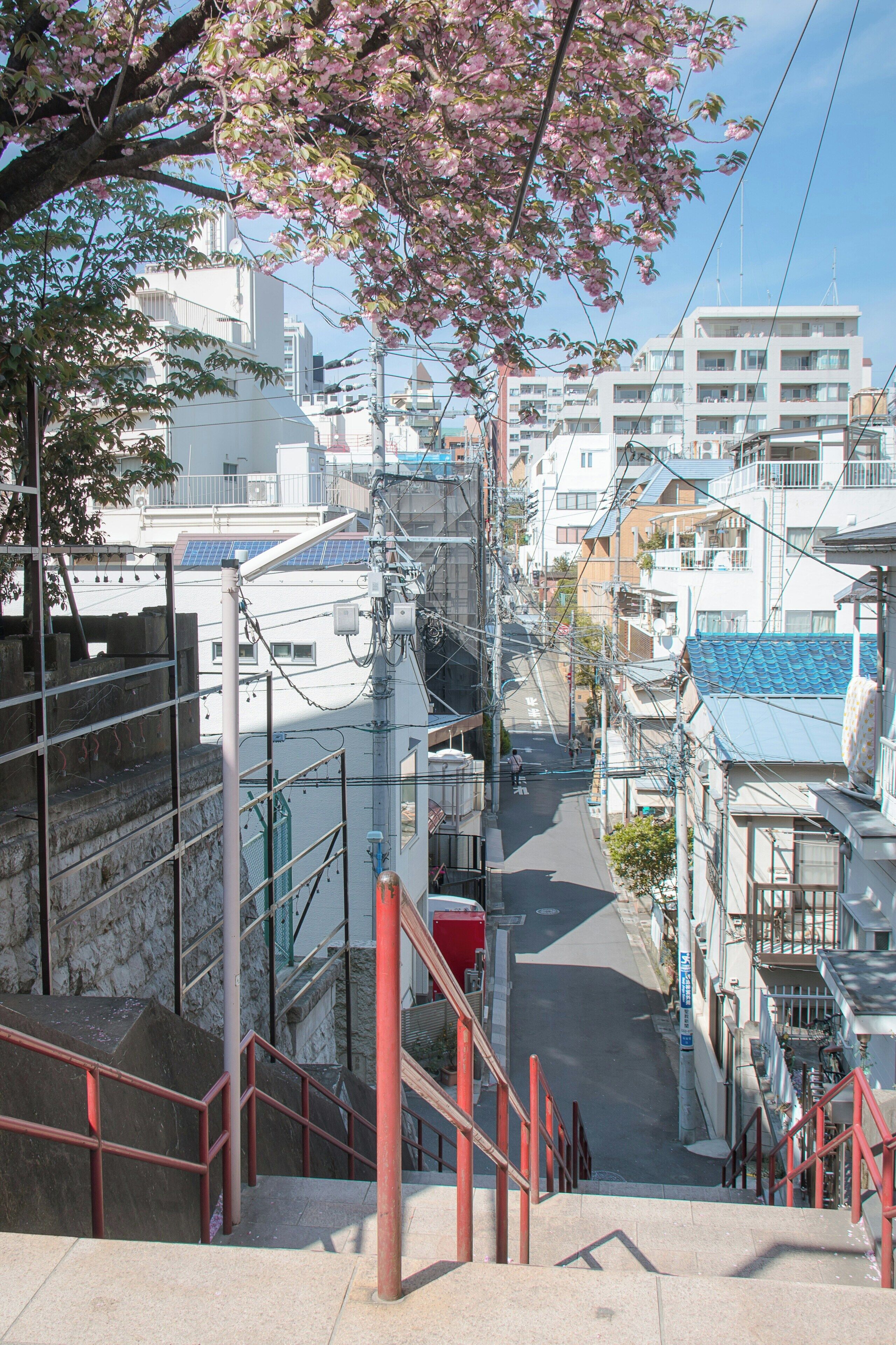 A narrow urban street with a staircase leading down to a lower level, surrounded by residential buildings and utility poles.