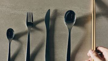 A set of black cutlery including a spoon, fork, knife, and chopsticks, arranged on a textured surface.