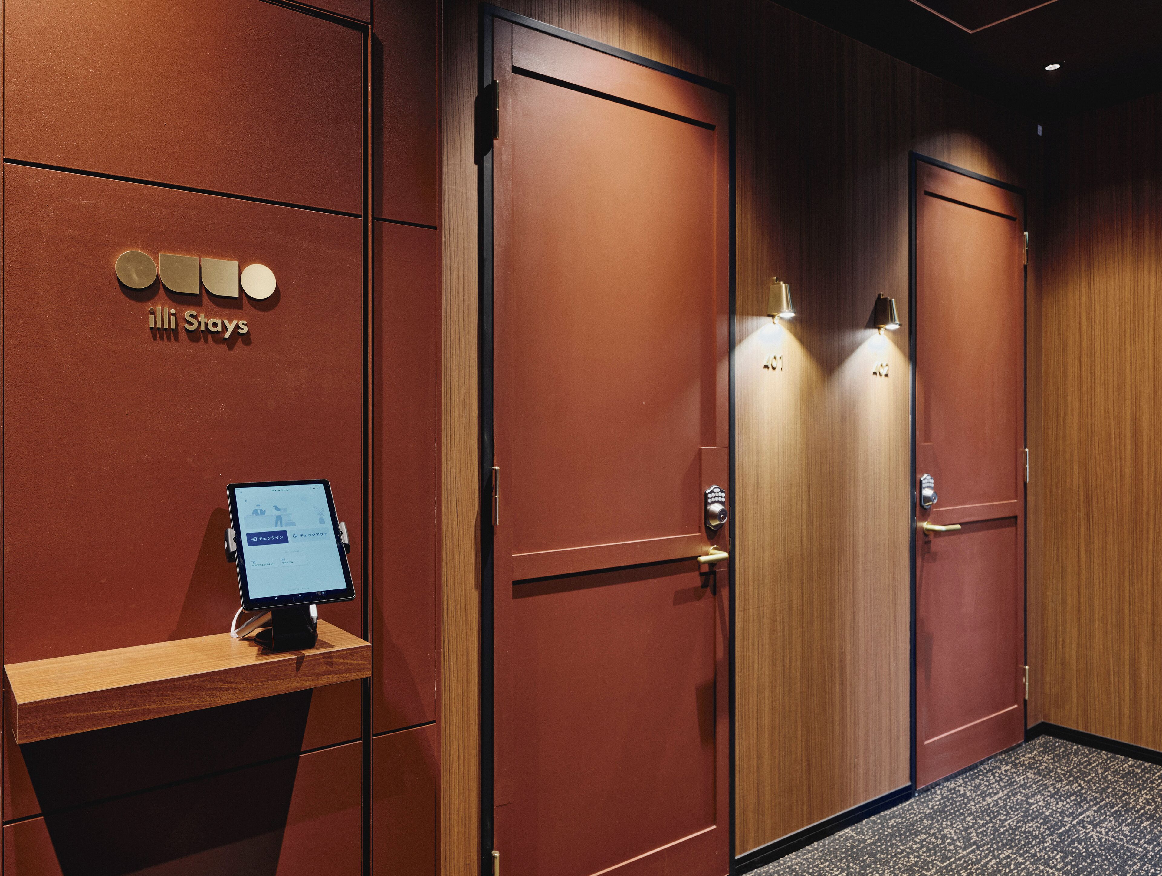 Ein Hotelzimmer mit Holztür, einer Rezeption mit Computer und einem Schild mit der Aufschrift "iLLi Stays".