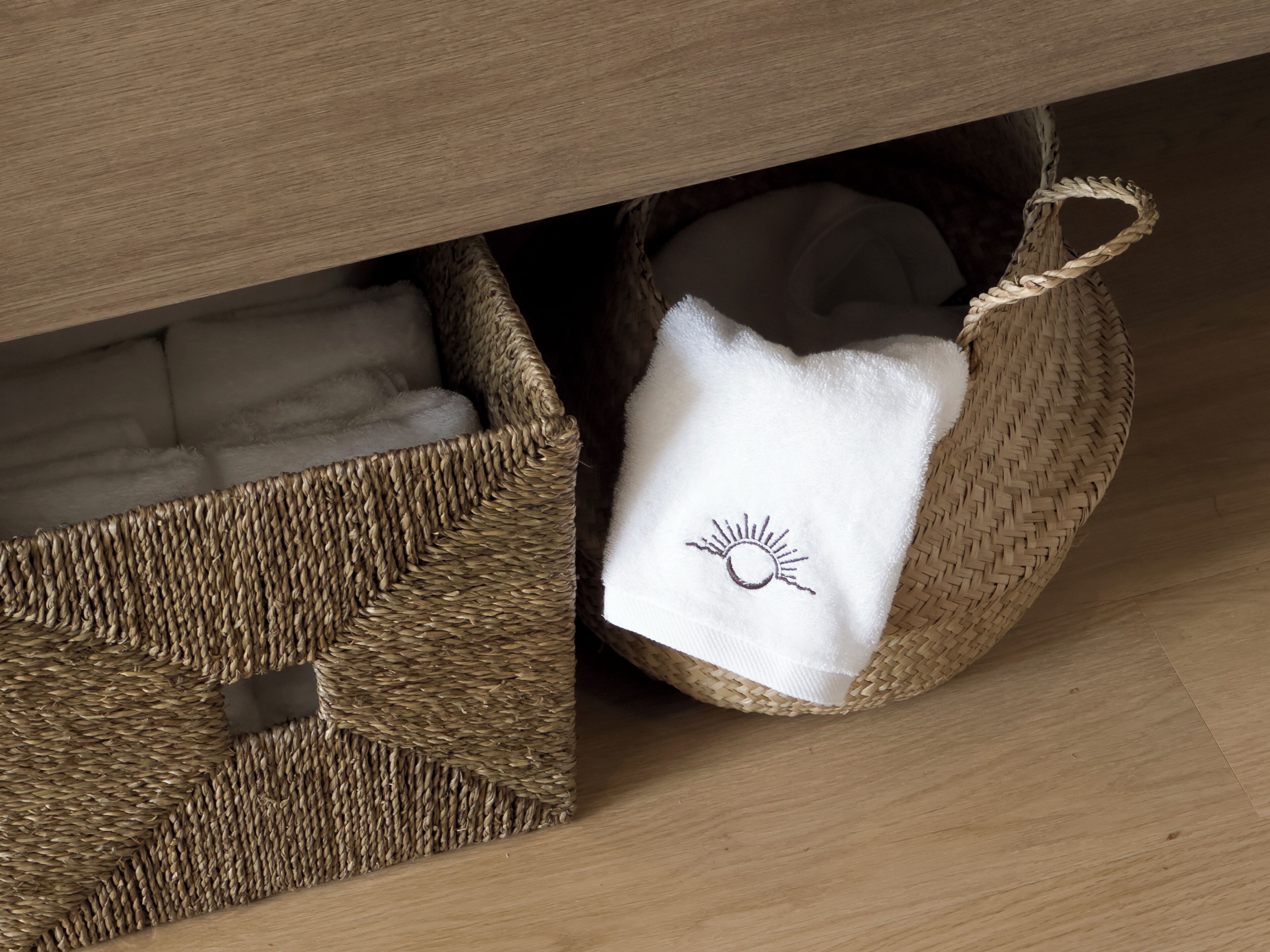 A wicker basket under a wooden cabinet with a white cloth featuring a sun design.