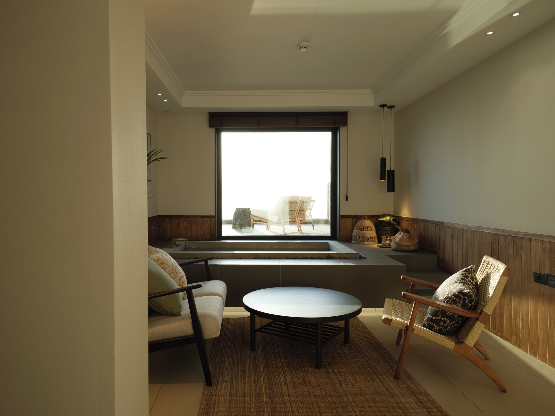 Una sala de estar moderna con un sofá, una mesa redonda y una silla. Una ventana grande ofrece vistas al exterior.