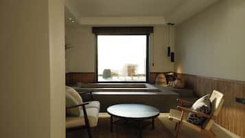 Una sala de estar moderna con un sofá, una mesa redonda y una silla. Una ventana grande ofrece vistas al exterior.