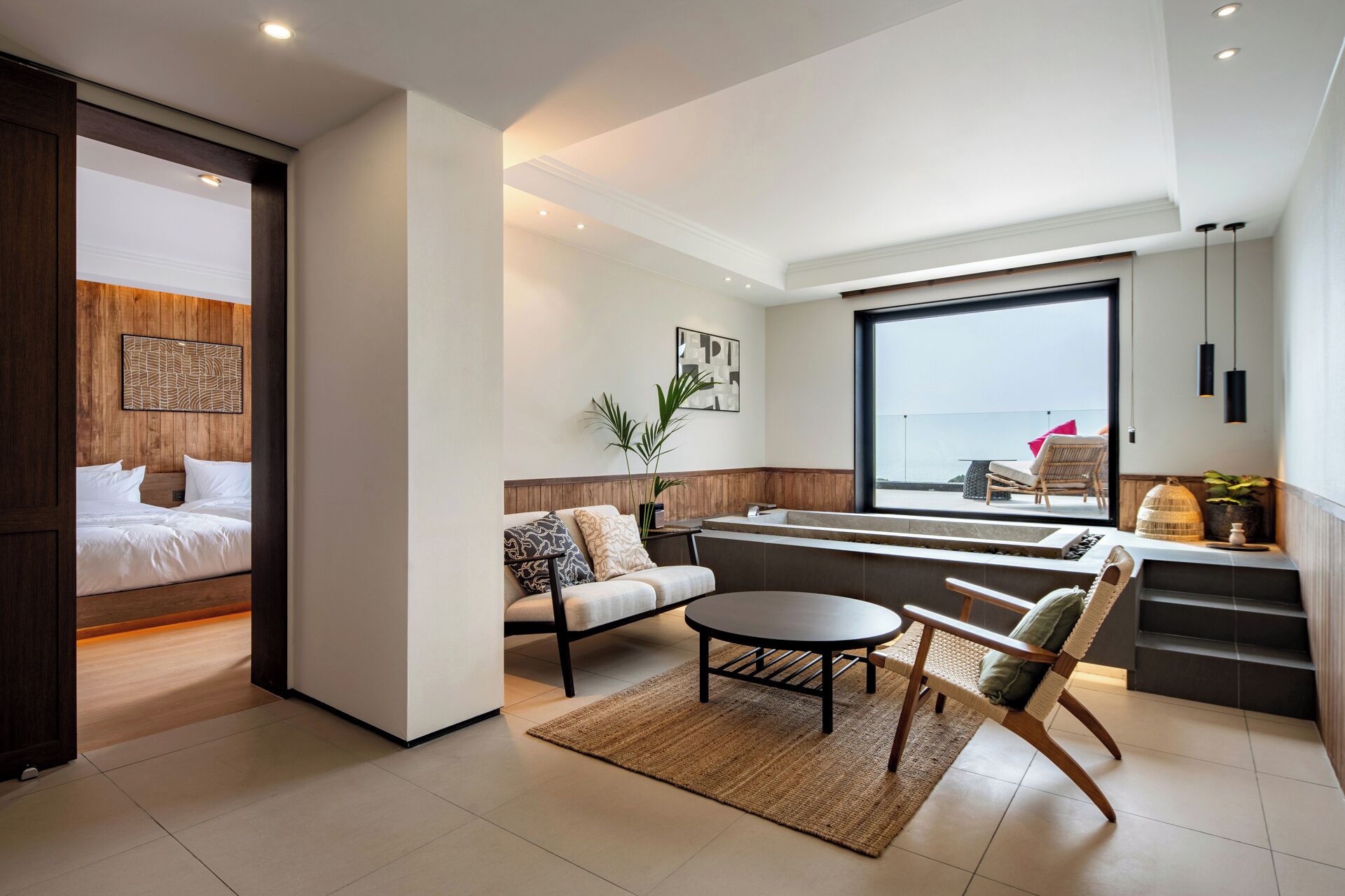A modern hotel room with a bed, seating area, and a view of the sea.