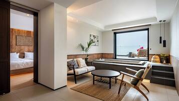 A modern hotel room with a bed, seating area, and a view of the sea.