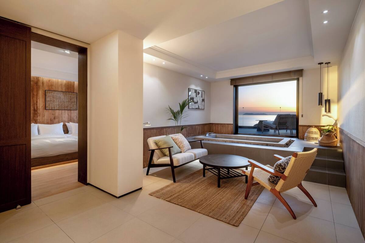 Una habitación de hotel moderna con cama, sofá, mesa de comedor y vista al mar.