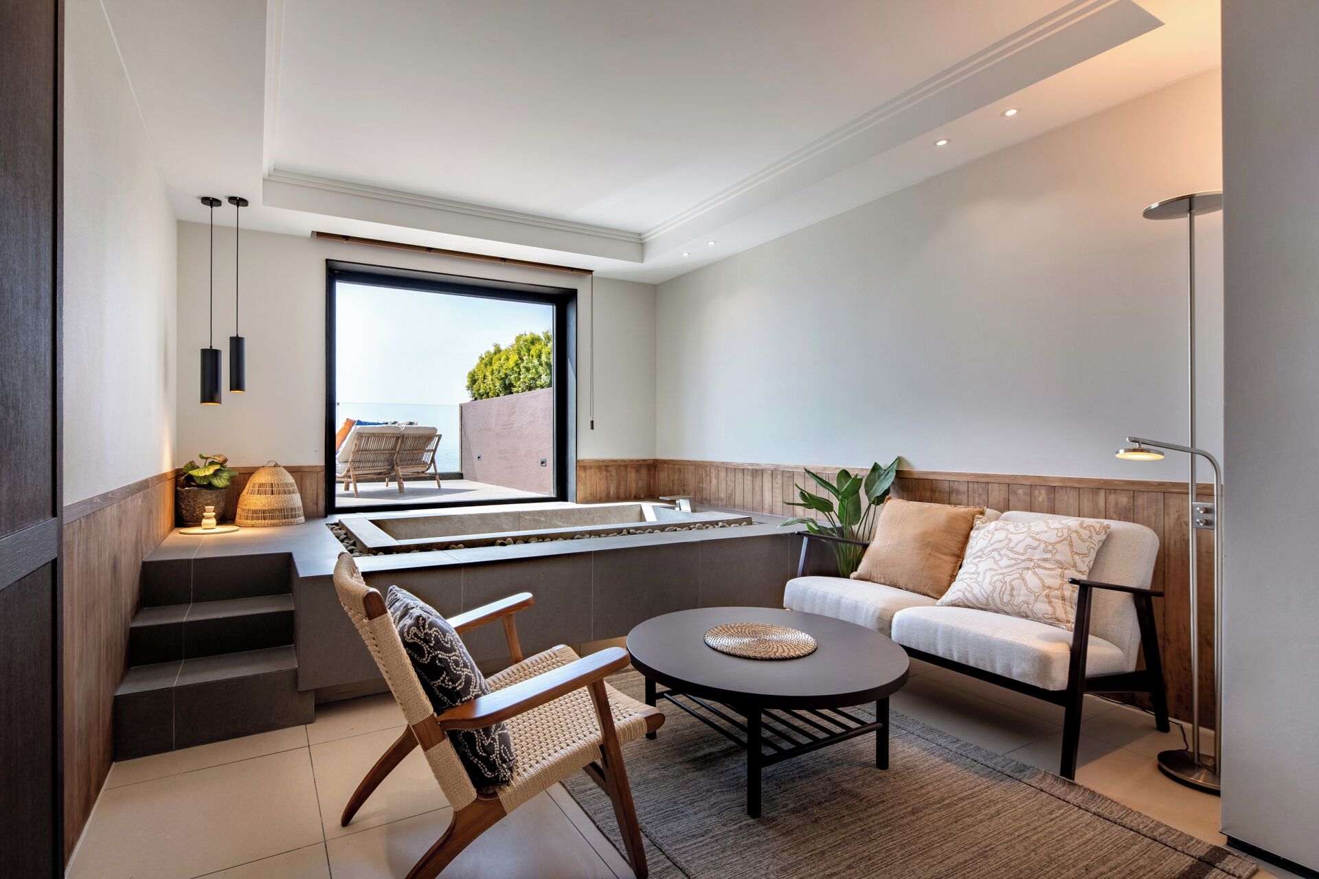 Una sala de estar moderna con un sofá, una mesa de centro, una silla y vistas al exterior a través de un ventanal grande.