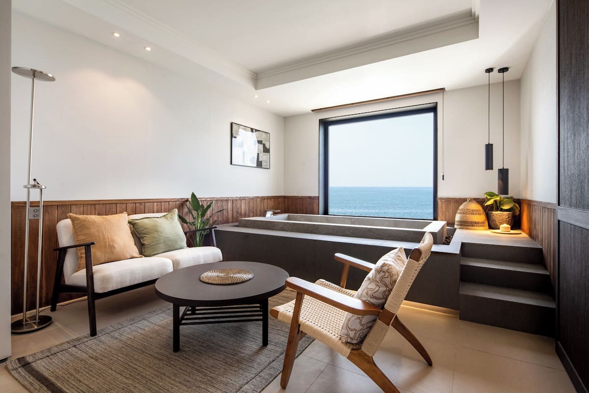 Una sala de estar moderna con un sofá, un sillón, una mesa de centro y un ventanal con vistas al mar.
