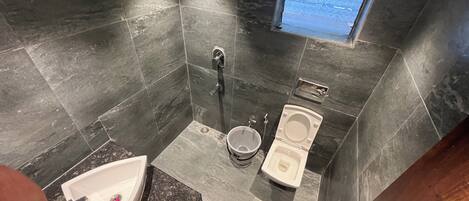 A modern bathroom with dark tiles, a shower, a toilet, and a sink.