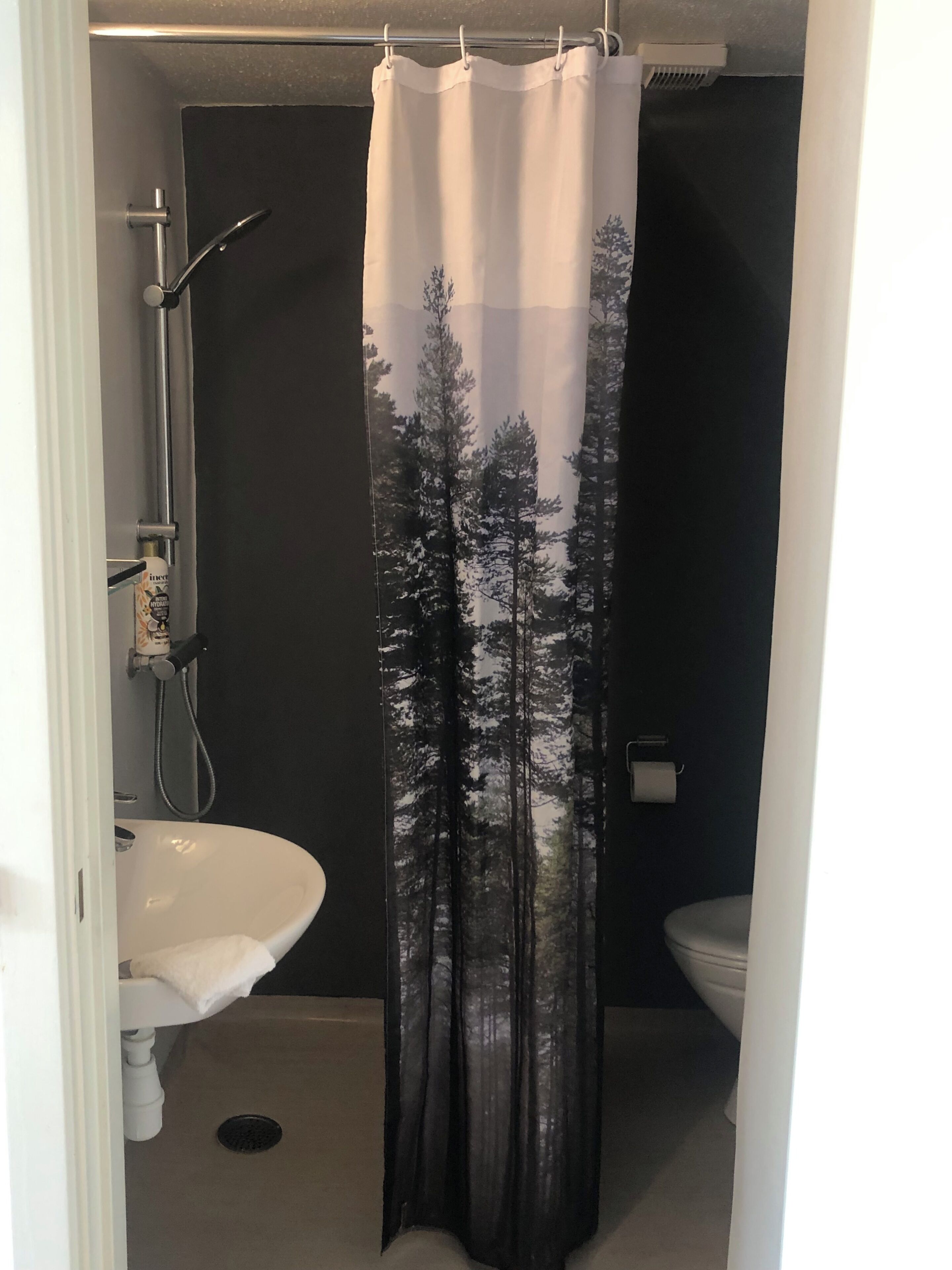 A bathroom with a shower curtain featuring a forest print, a white sink, and a toilet.