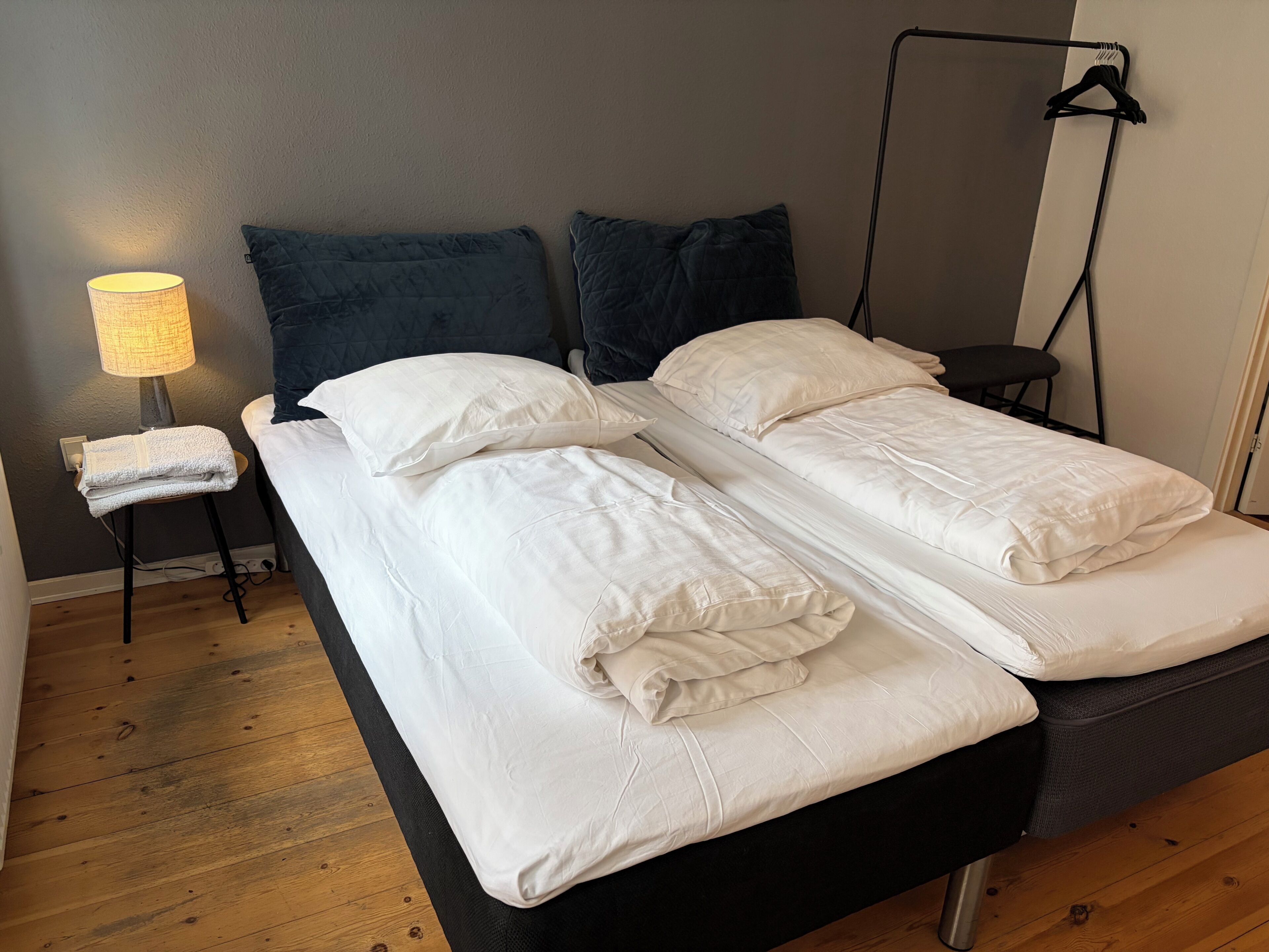 Un lit double avec du linge de lit blanc, une table de chevet avec une lampe et une chaise noire.