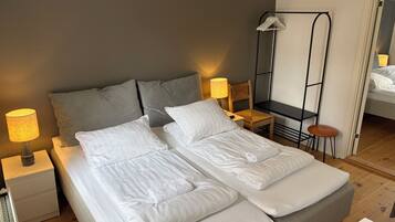 A double bed with white linens, two bedside tables with lamps, a wooden chair, and a small stool.