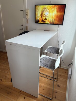 A compact room with a white desk, a chair, a television on the wall, and a wooden floor. - Huset ved springvandet (Randers)