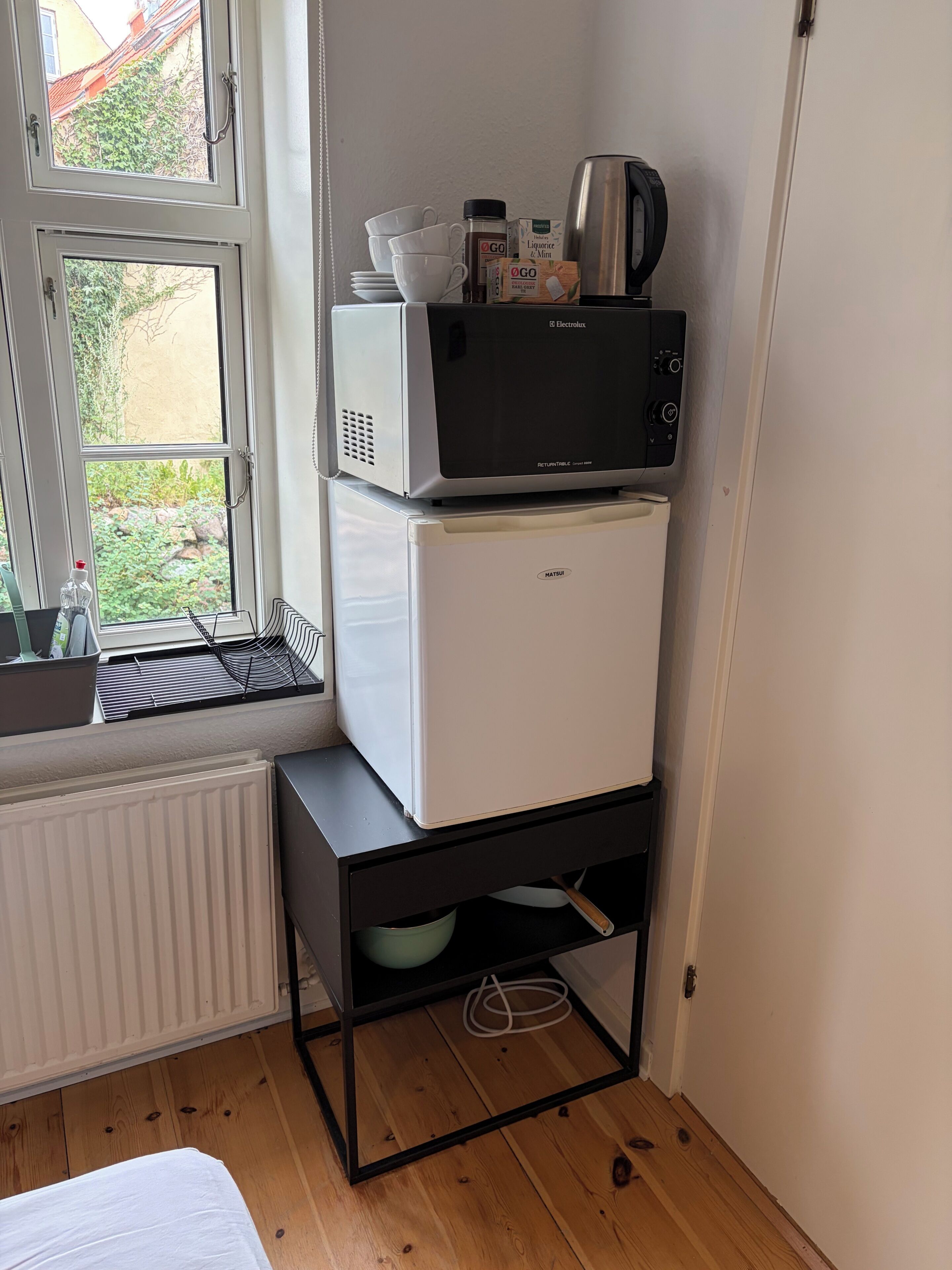 Et lille tekøkken med en mikrobølgeovn, køleskab og kaffemaskine på en sort metalkasse.