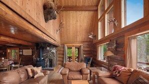 Ein rustikales Blockhaus-Interieur mit Kamin aus Naturstein, Ledermöbeln und aufgehängten Tierköpfen.
