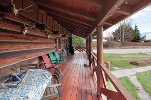 Une véranda couverte, dotée de bancs en bois et d’une table, décorée de bois de cerf.