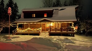 Eine Blockhütte mit schneebedecktem Dach, einer Veranda mit Lichterketten und einer Holzterrasse.